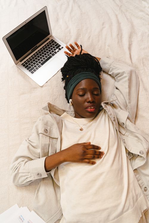 Free A woman rests peacefully on a bed beside her laptop, depicting a moment of relaxation. Stock Photo