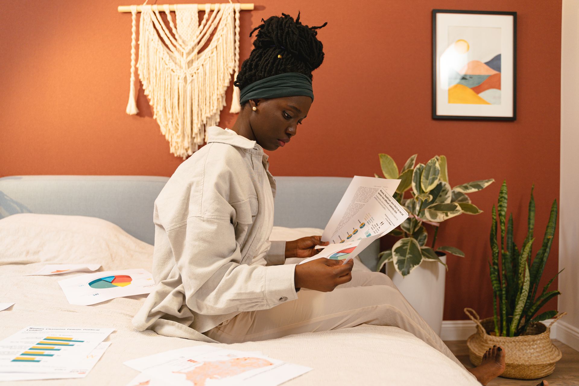 A young woman analyzes documents in a stylish bedroom, focusing on graphs.