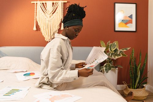Free A young woman analyzes documents in a stylish bedroom, focusing on graphs. Stock Photo