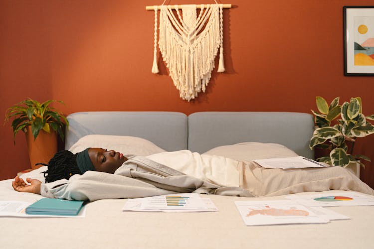 A Woman Lying Down On The Bed Surrounded With Scattered Papers