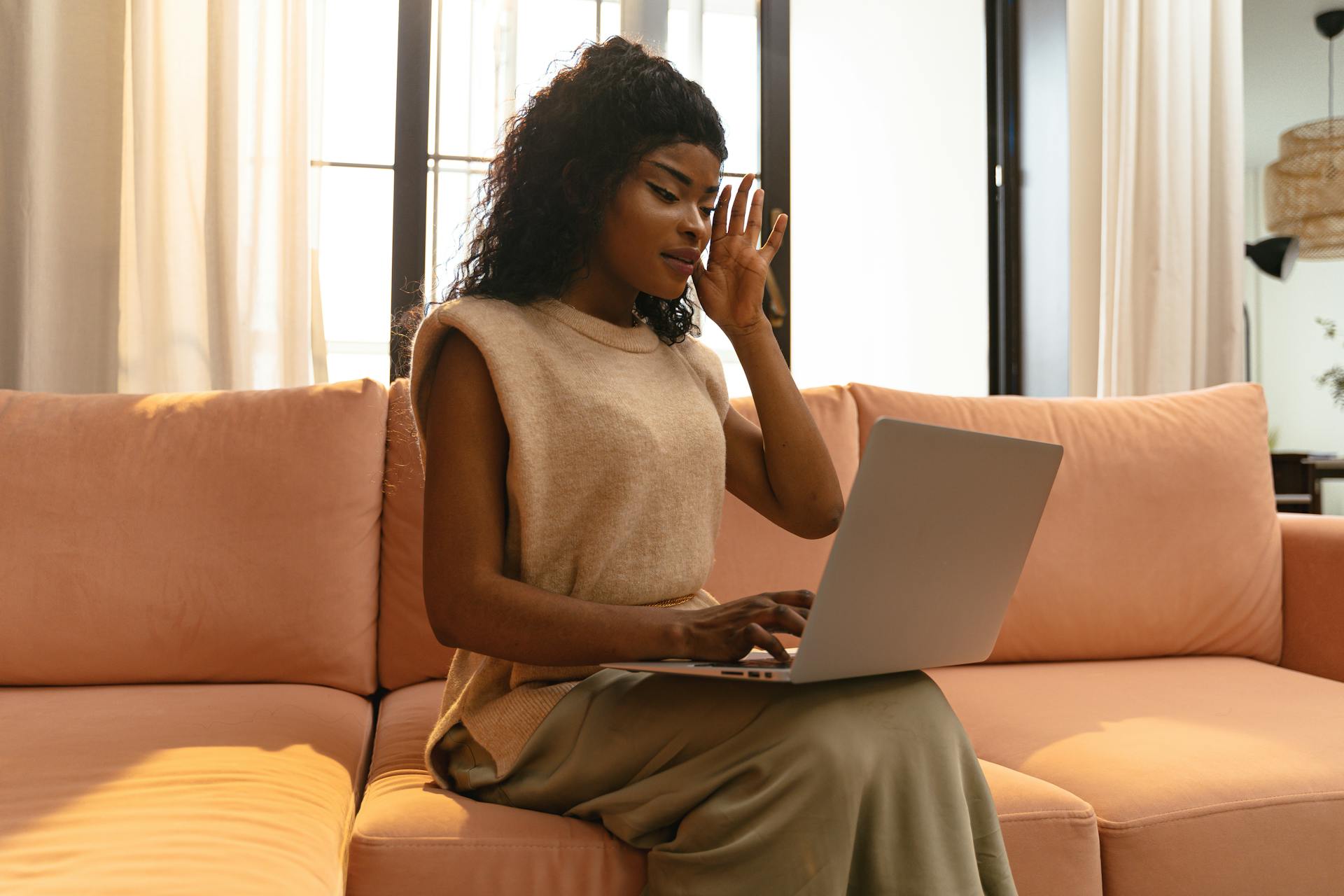 A young woman sits on a modern sofa using a laptop in a cozy home interior.