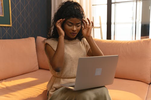 Young Woman Sitting on a Couch and Using Laptop and Touching Her Temples From a Headache 