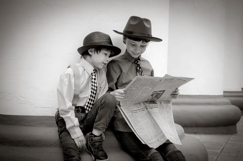 Free Two young boys in hats and ties reading a newspaper evoke a classic, vintage style. Stock Photo