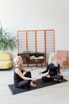 Two senior women practicing meditation on yoga mats in a calm indoor setting.