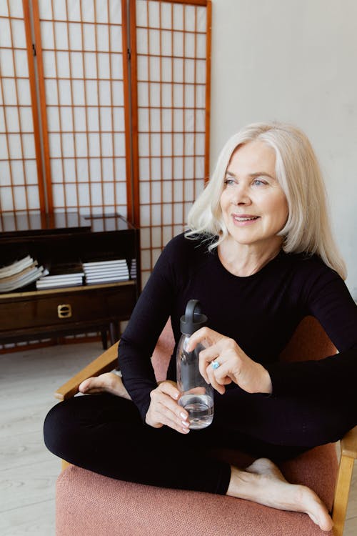 Woman in Black Long Sleeves Holding a Tumbler Sitting on a Chair while Looking Afar