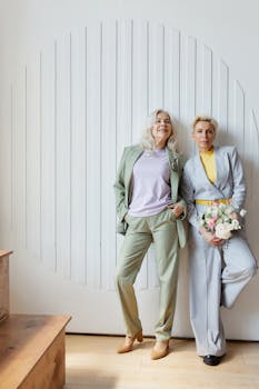 Two stylish adult women in suits posing with a bouquet indoors, showcasing elegance and friendship.