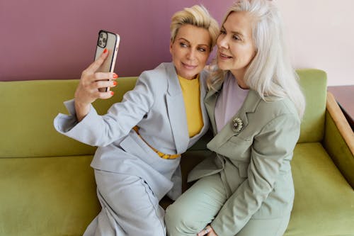 Woman in Gray Blazer Holding Iphone Beside Woman in Green Blazer