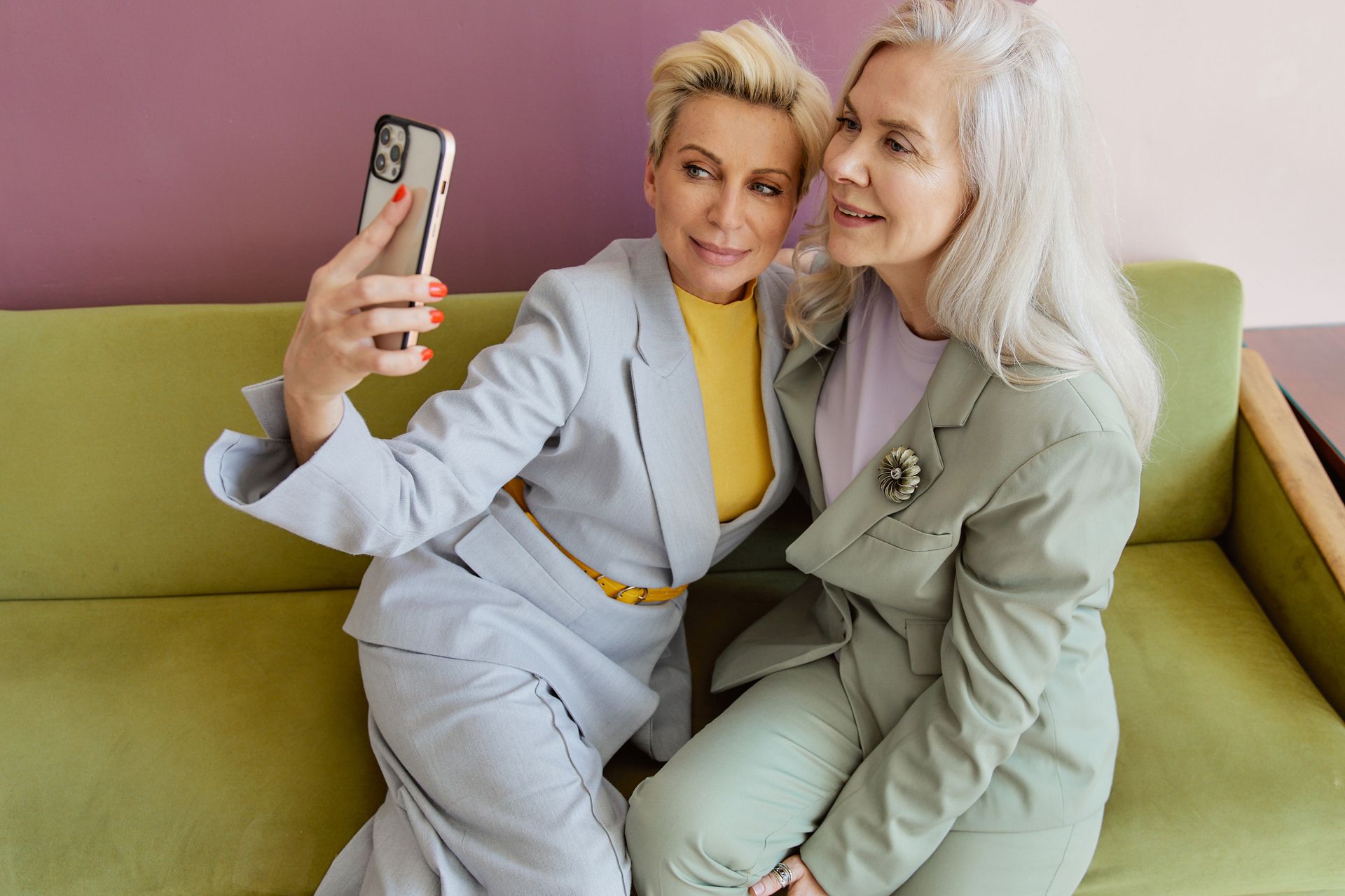 Two stylish women sitting on a couch, capturing a joyful selfie together.