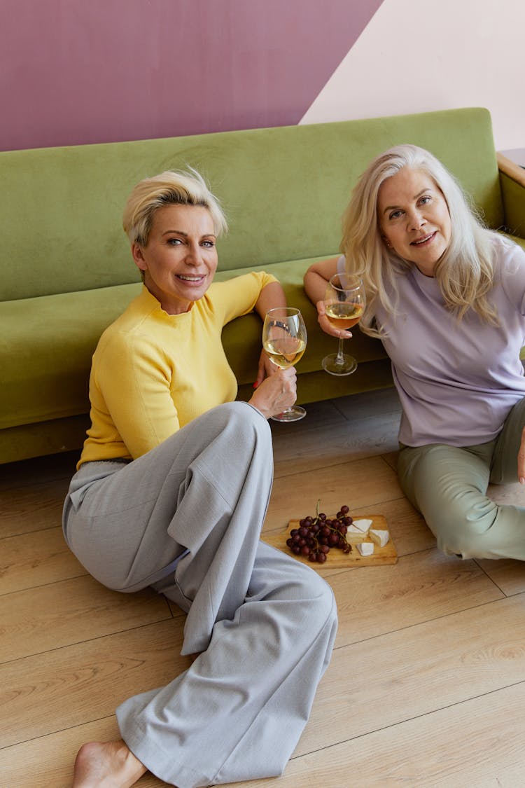 Mature Women Sitting On The Floor With Glasses Of Wine And A Snack 