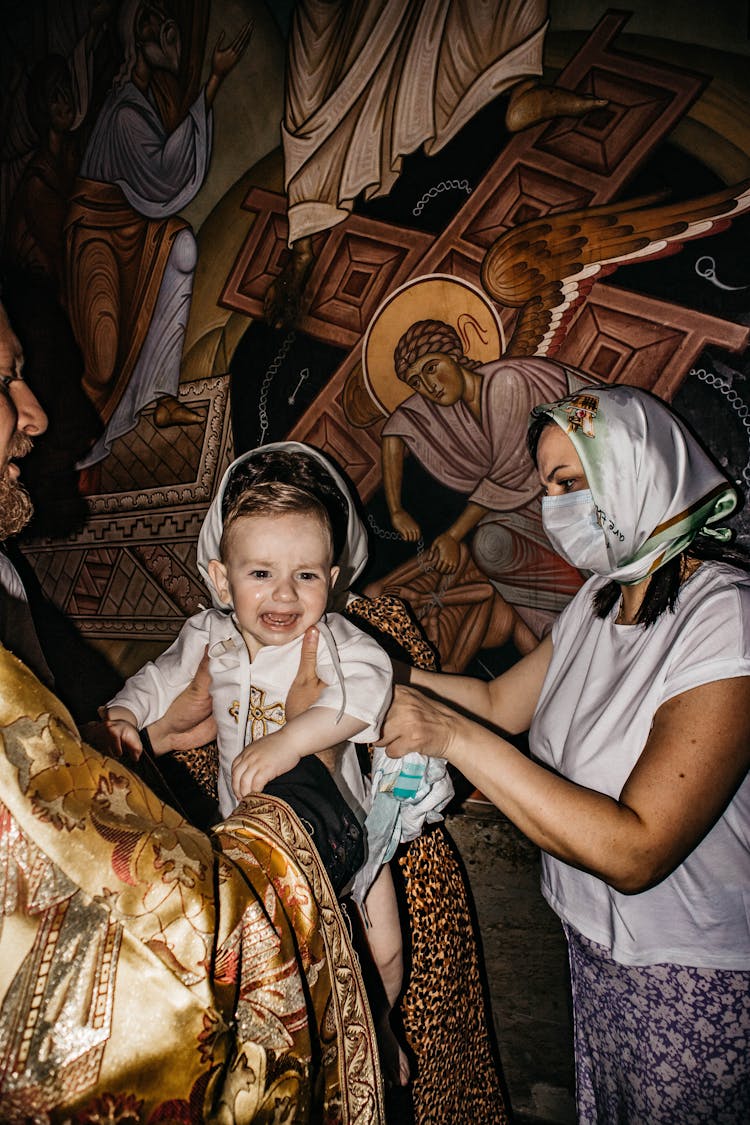 Priest Holding A Crying Baby Boy And Giving Him To His Mother 