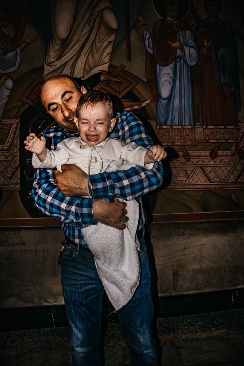 Free Asian father comforting crying toddler inside a religious building with wall art. Stock Photo