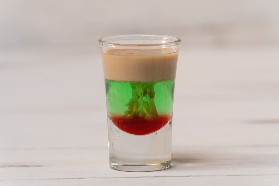 A small shot glass showing two distinct layers, amber butterscotch schnapps on the bottom and pale cream-colored Irish cream floated on top, on a dark bar surface.