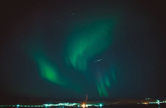 Stunning aurora borealis with vibrant green hues illuminating a starry night sky over a tranquil landscape.