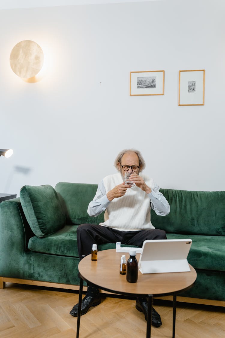 A Man Sitting On Green Couch Drinking Water