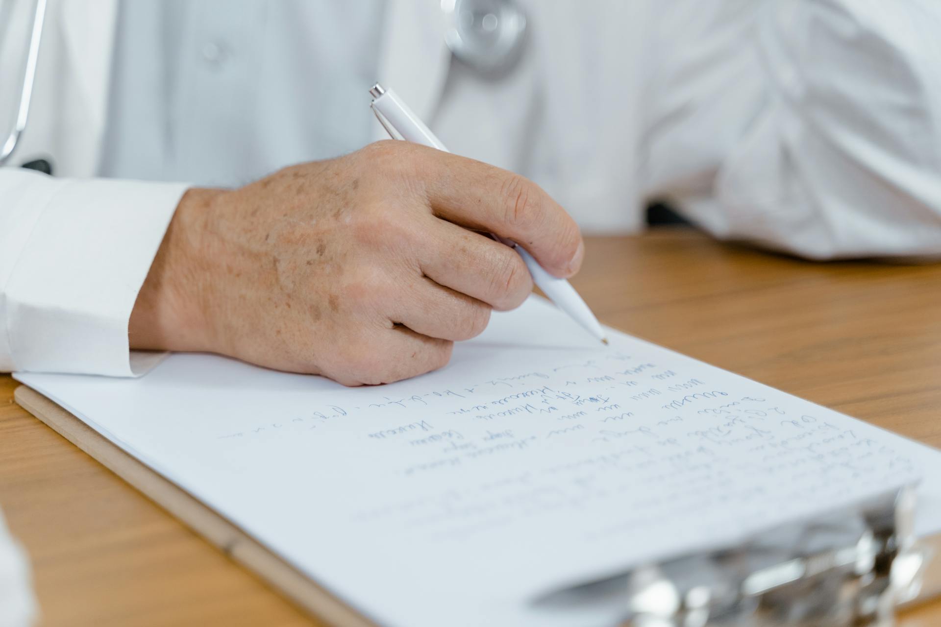 Close-up of a doctor's hand writing notes with a pen on paper, capturing a moment in a medical setting.