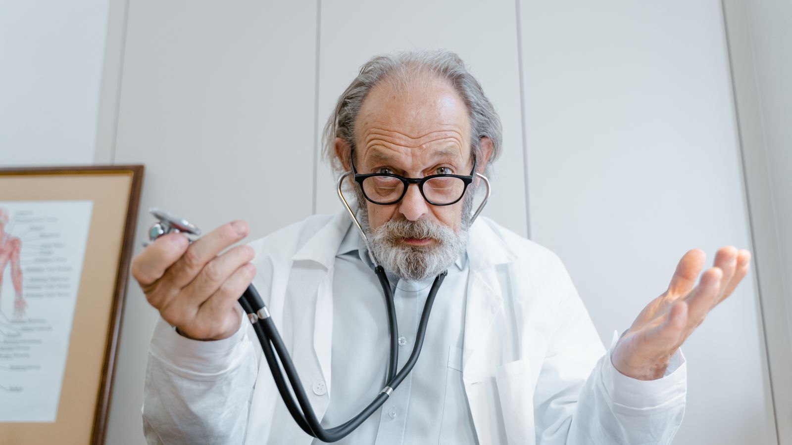 Senior doctor gesturing with stethoscope in a clinical setting, emphasizing telemedicine.
