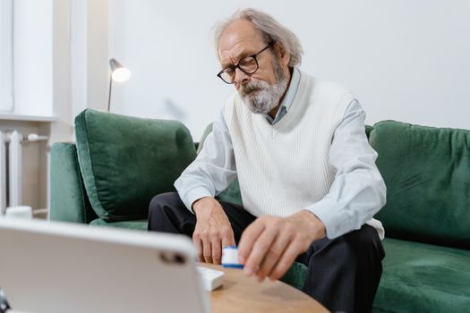 Elderly man with glasses using a tablet for telehealth consultation at home.