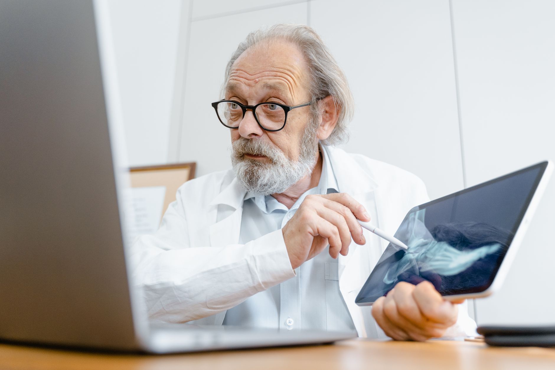 A physician at a clinic desk consulting a digital interface that shows an AI-generated diagnostic suggestion alongside a clinical guideline, the human reviewing and editing before signing off.