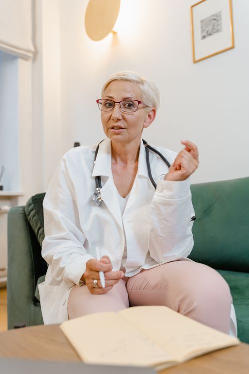 Free Senior female doctor with eyeglasses and stethoscope sitting indoors for consultation. Stock Photo