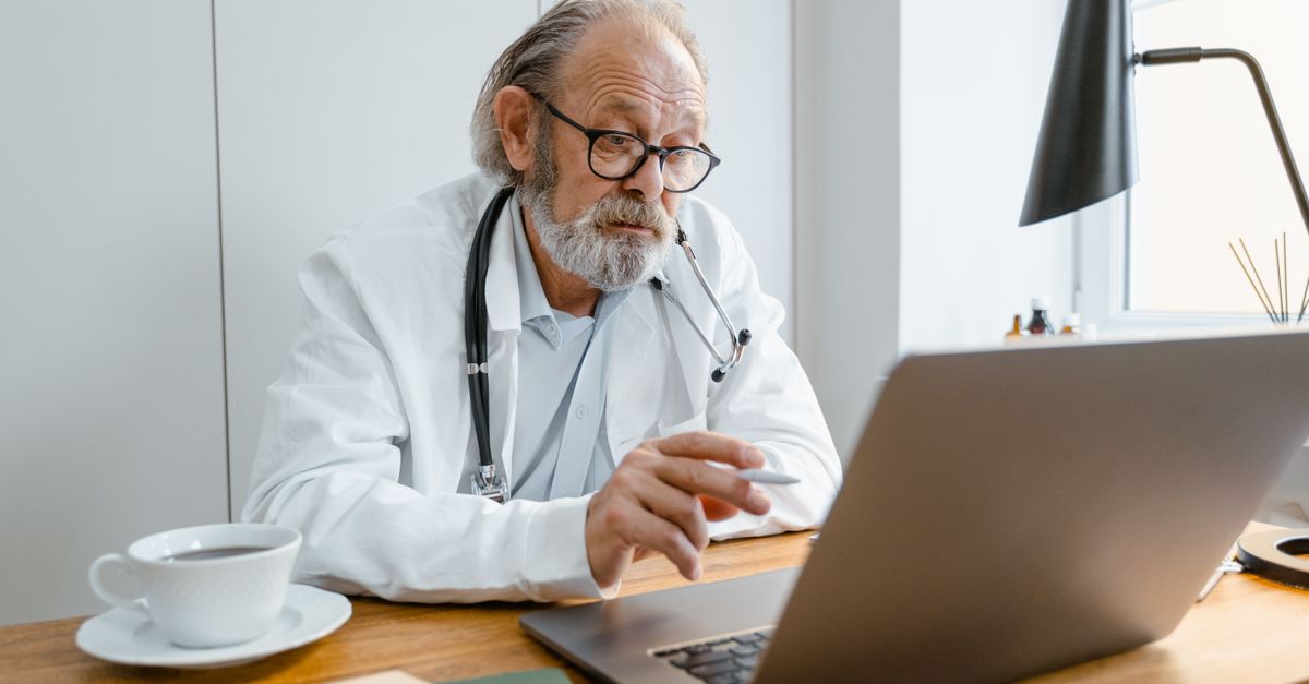 Senior male doctor using laptop for telehealth consultation in office setting, illustrating Is SilverSneakers Free With Medicare? â 1-800-MEDIGAP, America's Trusted Toll-Free Number.