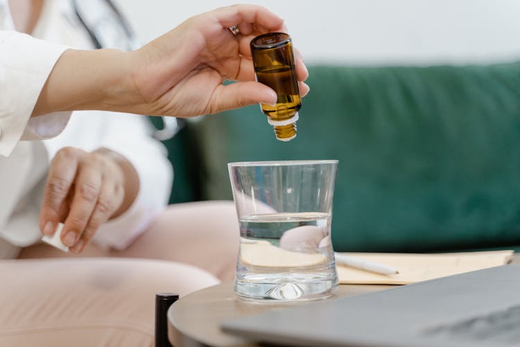 Close-Up Shot Of A Person Pouring Essential Oil In The Glass Of Water