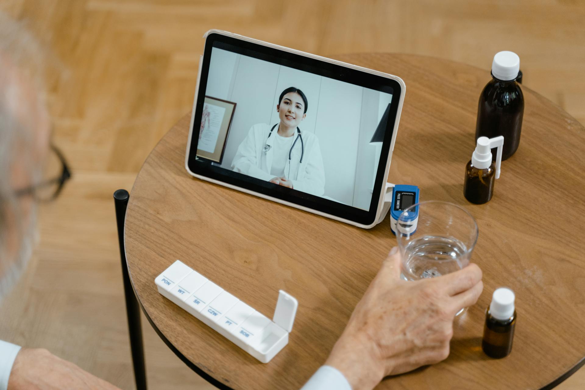 Senior adult having a virtual doctor consultation on a tablet with medications on the table.