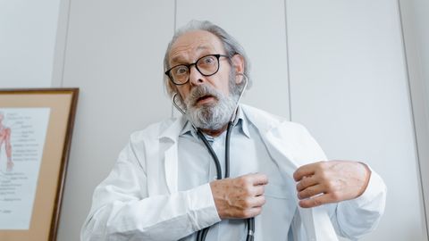 Surprised elderly doctor wearing lab coat and stethoscope indoors.