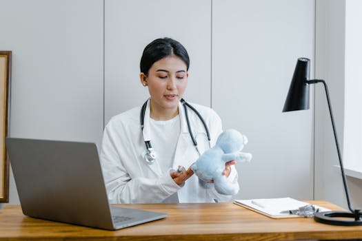 Female doctor in office holding teddy bear during a video call session.