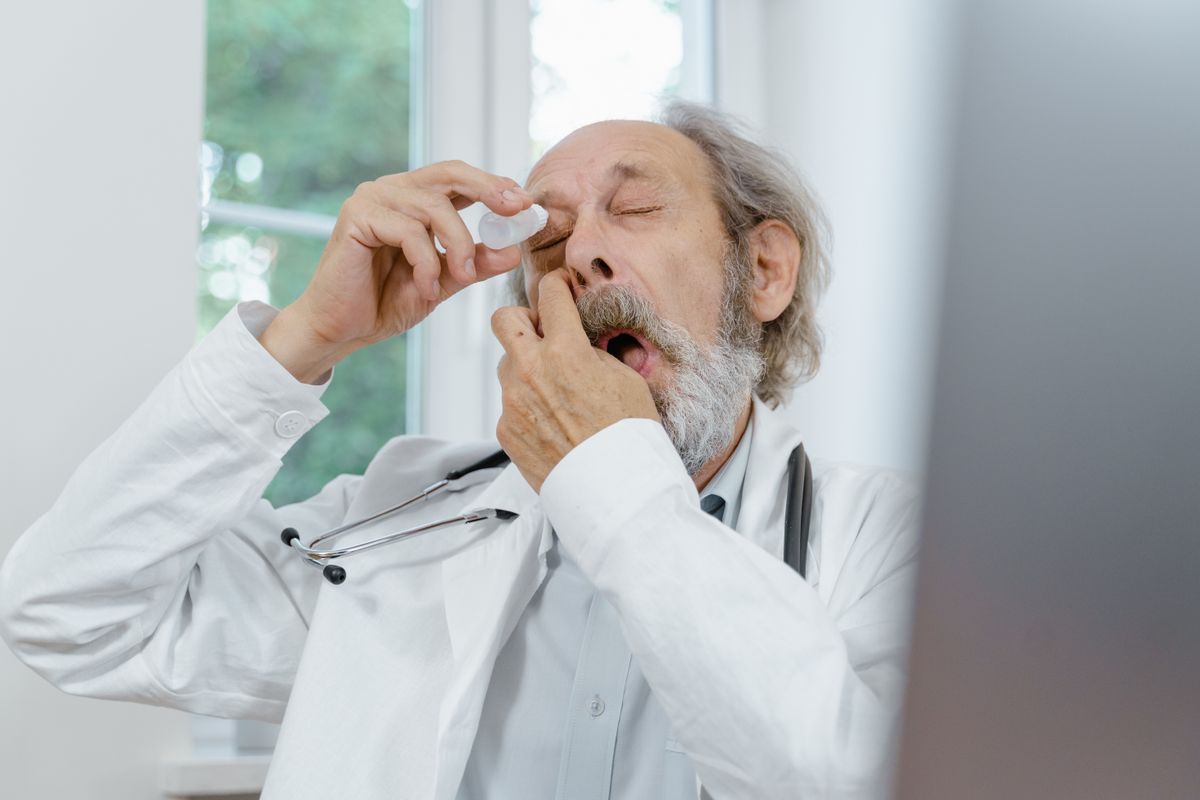 Older man carefully applying eye drops during recovery