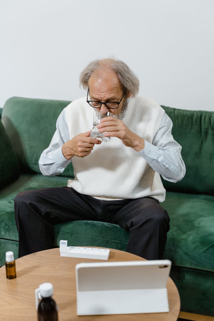 Elderly Man Taking His Medicine While Sitting On Green Couch