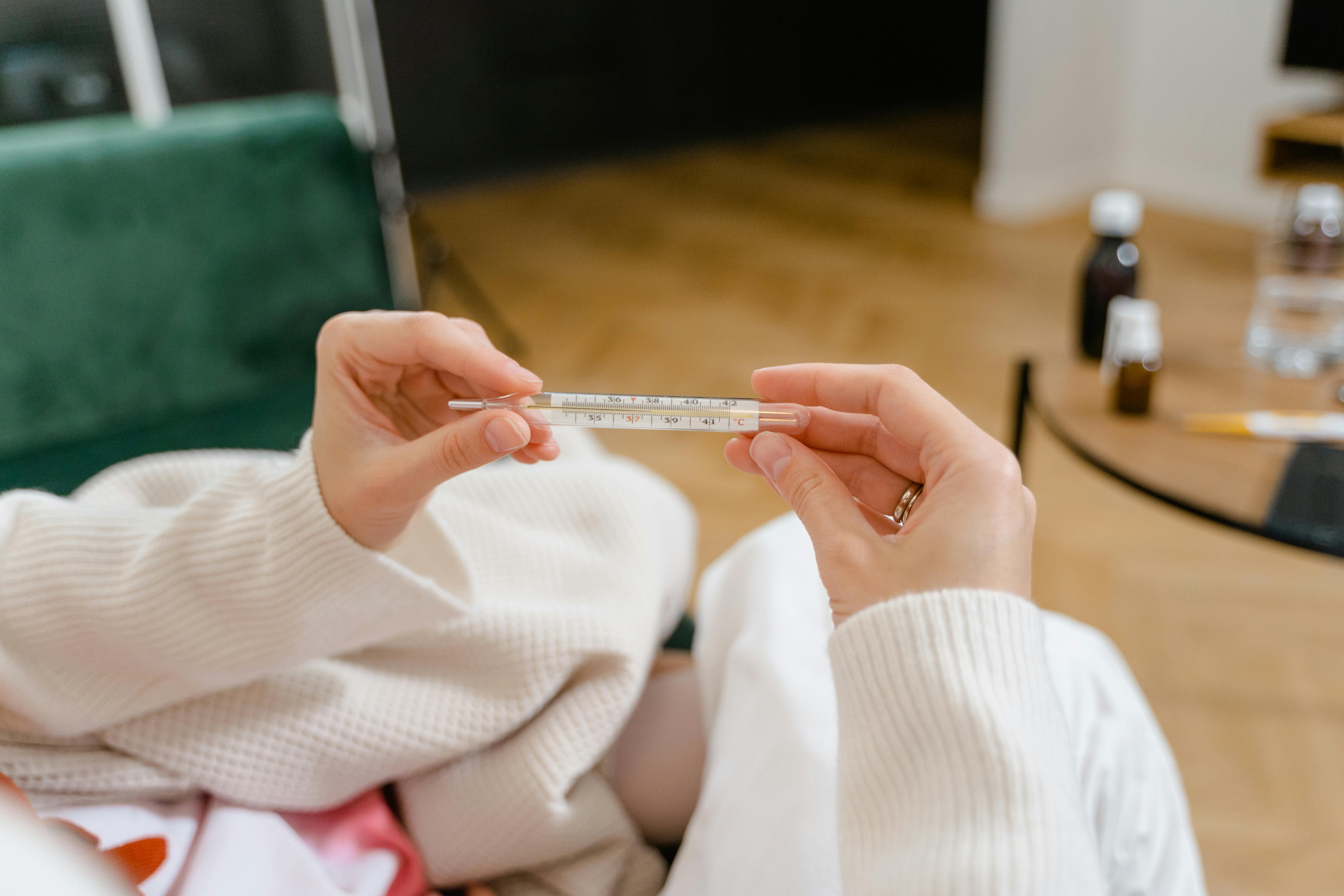 Adult hands holding a glass thermometer indoors, shallow focus on healthcare context.