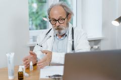 An elderly doctor in a white coat conducting an online medical consultation, focusing attentively.