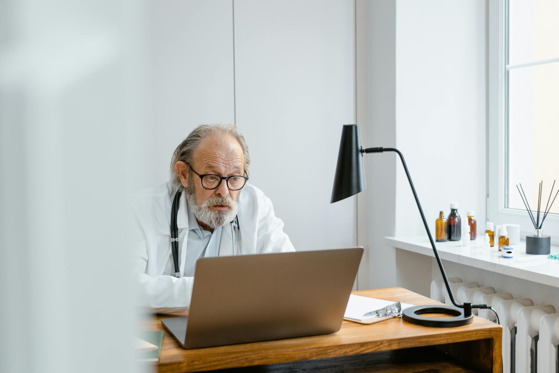 Senior doctor using a laptop for telemedicine in a modern office setting.