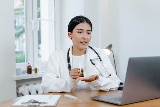 A young female doctor in a white coat on a video call, discussing medication with a patient.