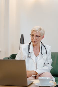 Senior female healthcare worker in a video call with a patient, wearing a stethoscope and lab coat.