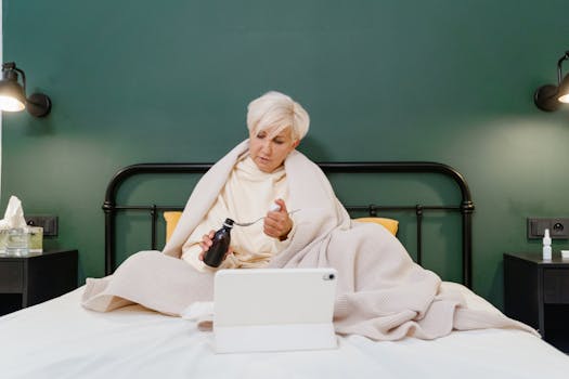 A senior woman sits on her bed using telehealth services during a pandemic, engaging with a health professional online.