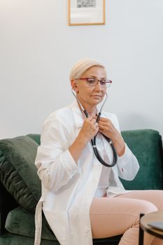 A female doctor in a white coat using a stethoscope in an office setting, telemedicine concept.