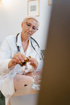 A female doctor with blond hair prepares medicine in a medical office, wearing eyeglasses and a stethoscope.