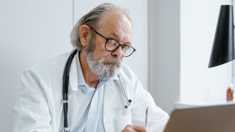 Elderly doctor using telemedicine for virtual consultation in office.