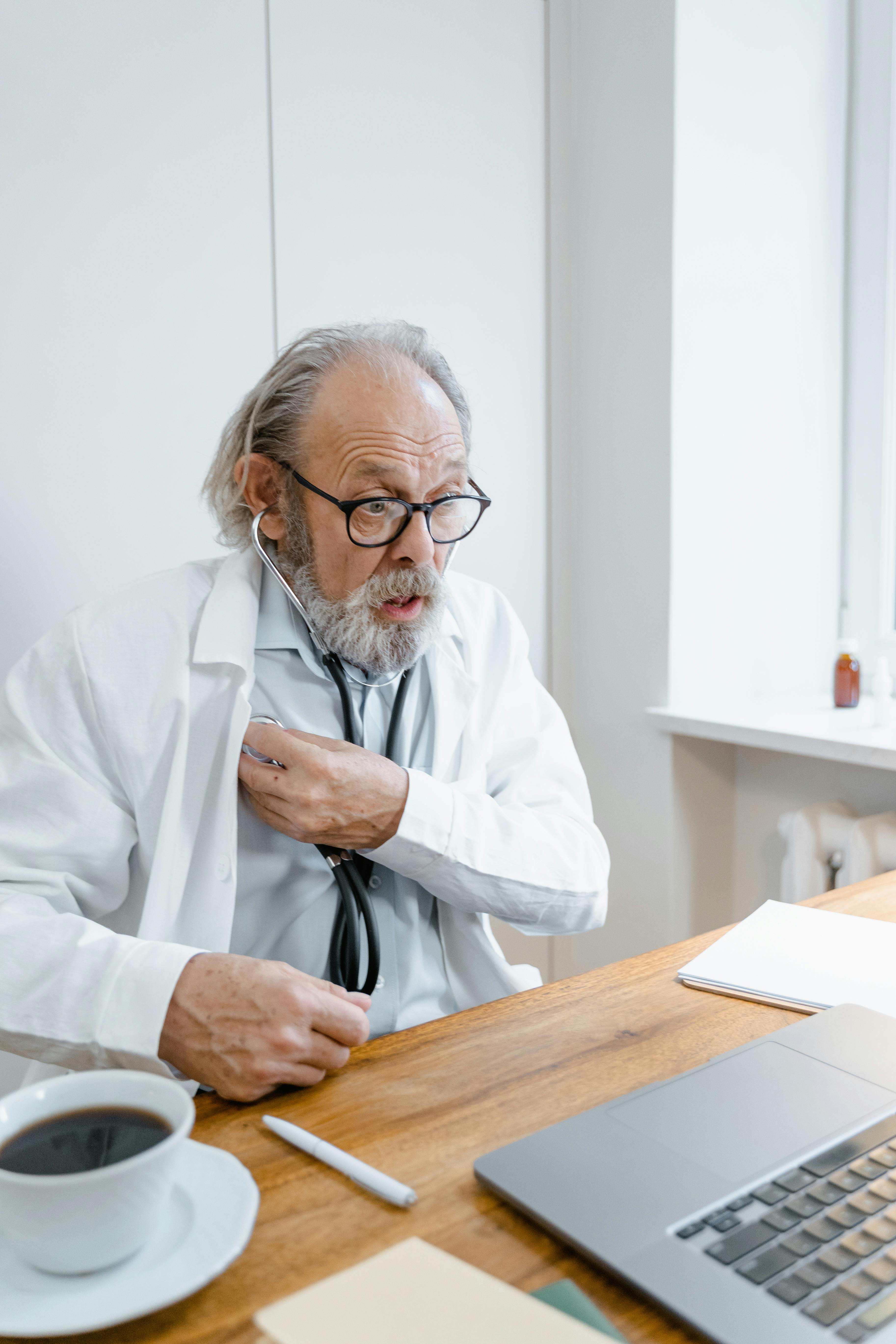 an elderly man using his stethoscope while talking in front of the laptop