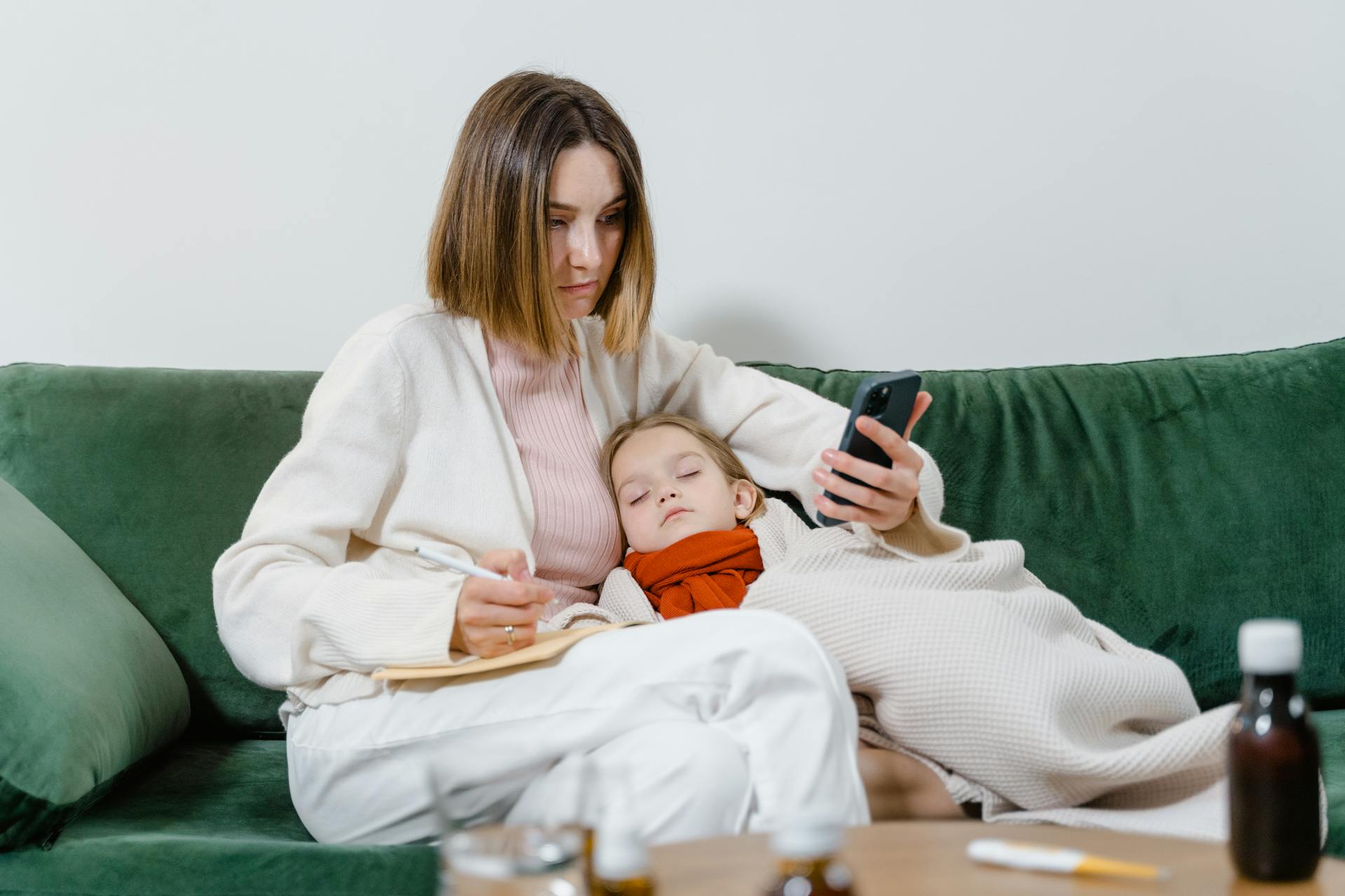 Woman Using Phone with Sick Child Sleeping in her Arms