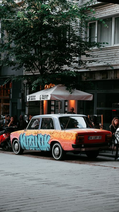 Free A classic car adorned with graffiti art parked on a city street outside a cafe. Stock Photo