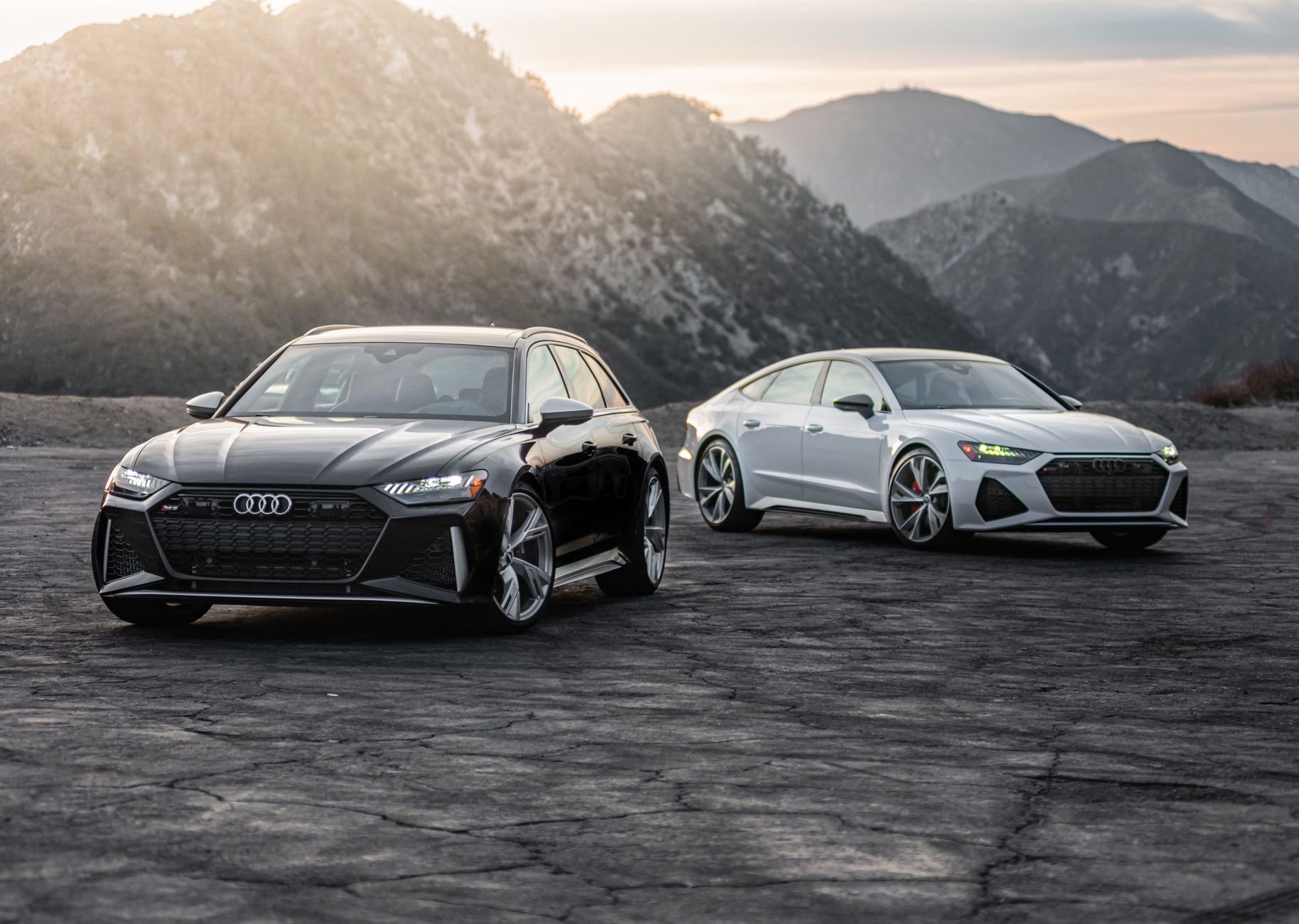 Two luxury Audi RS models parked on a scenic mountain road at sunset.