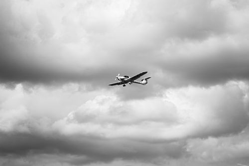 Free A small airplane flying amidst dramatic black and white cloudy skies. Stock Photo
