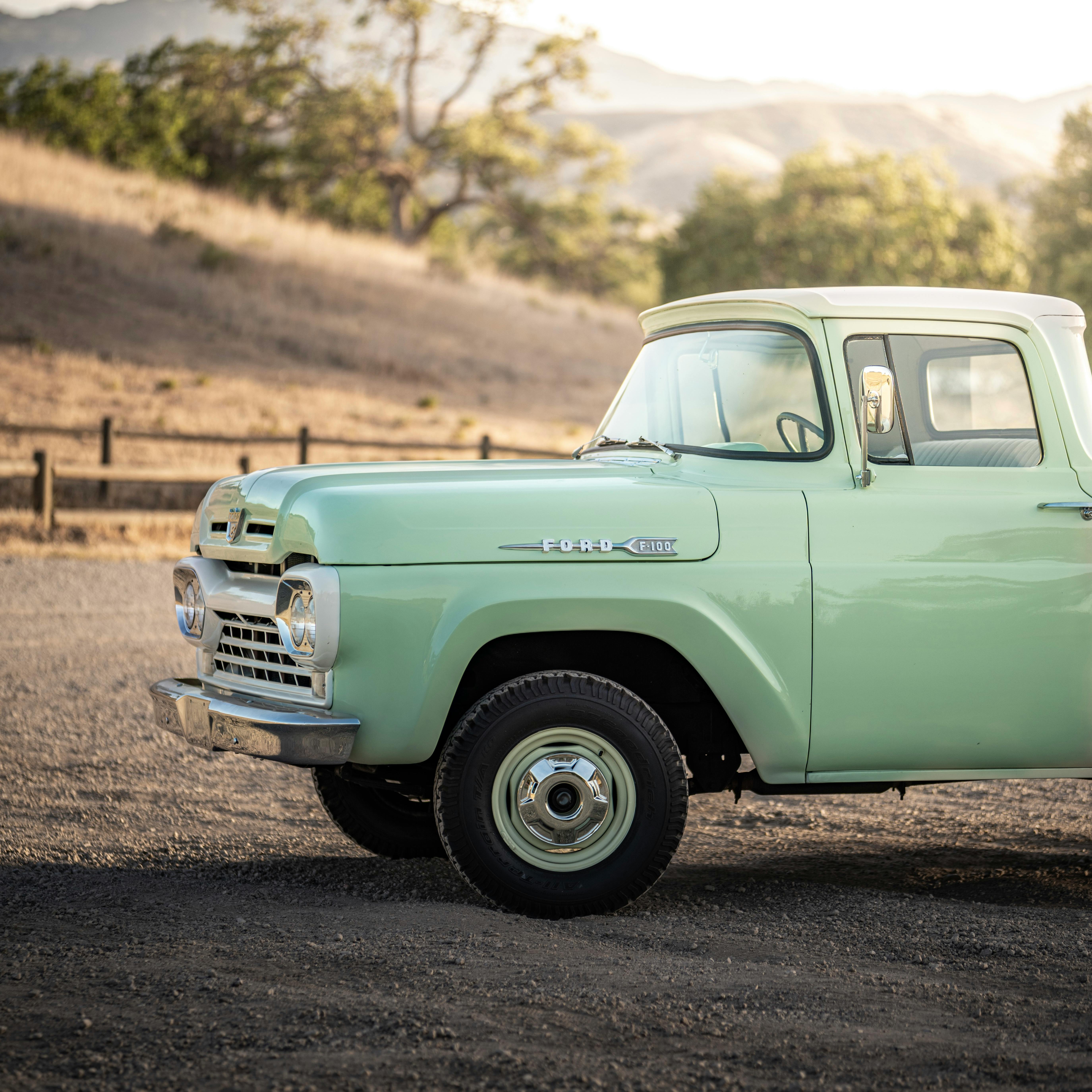 Vintage mint green Ford truck parked in a picturesque rural landscape during sunset.
