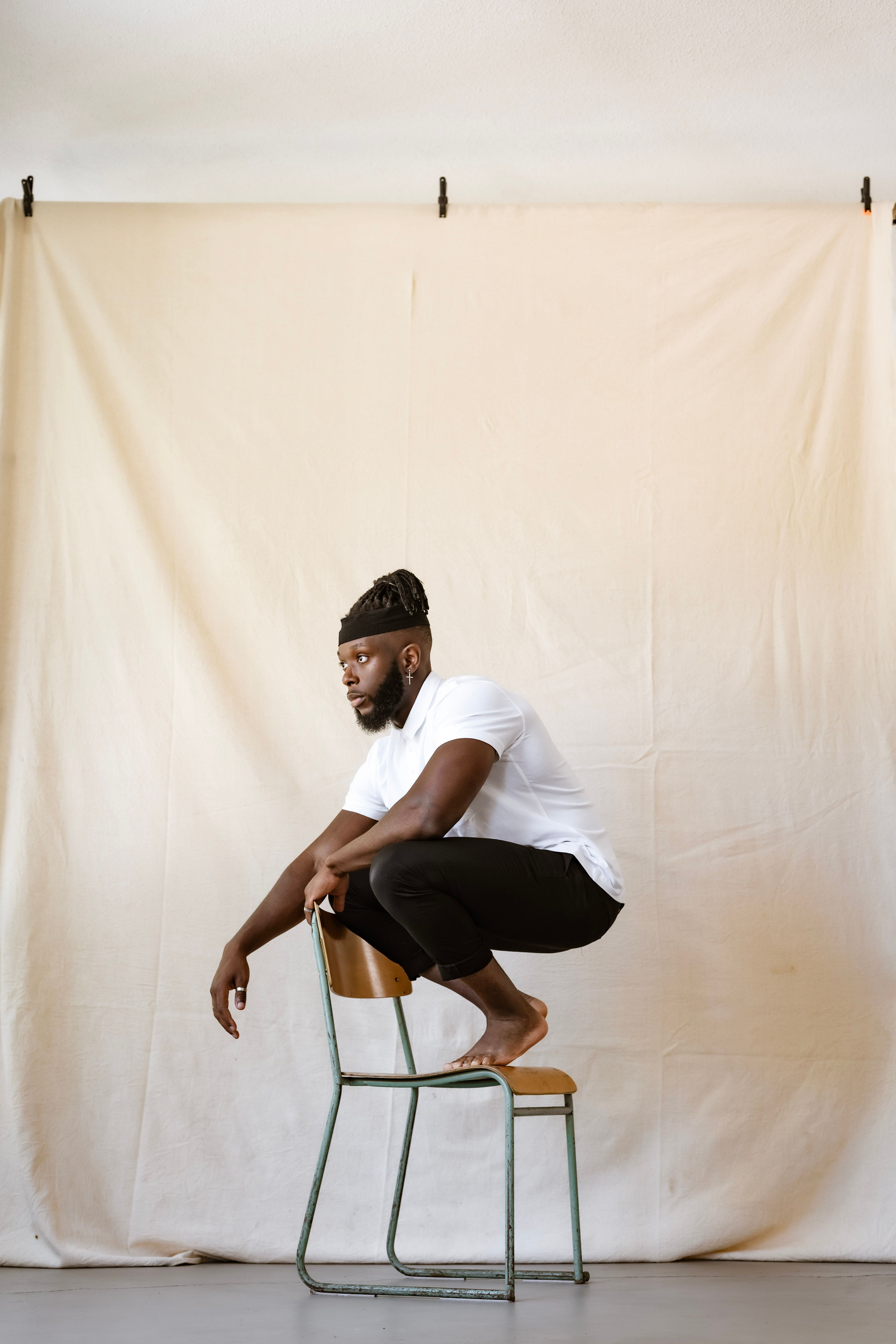 Adult man with dreadlocks poses on a chair in a modern minimalist studio.