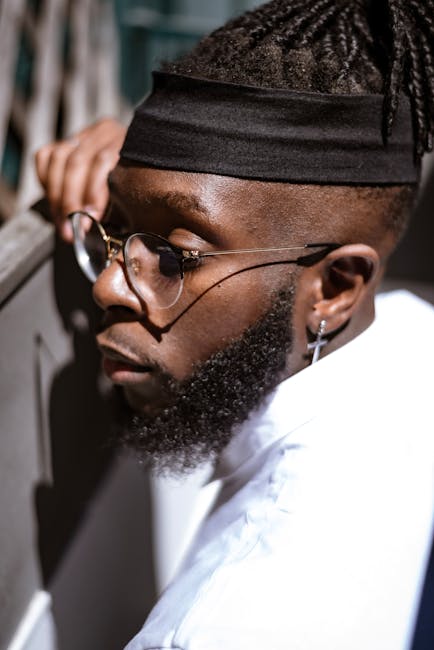 Close-up of a bearded man with eyeglasses and dreadlocks wearing a headband outdoors.