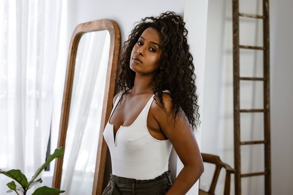 Portrait of a beautiful woman with curly hair in a white top posing indoors.
