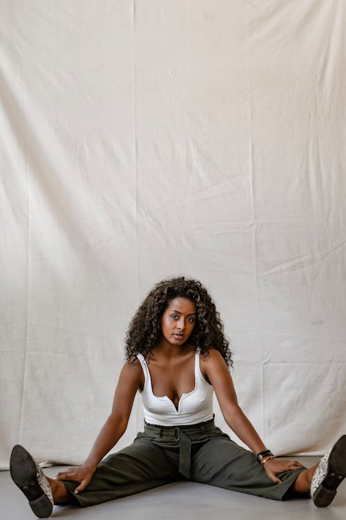 A Woman in White Sexy Top Sitting on the Floor while Posing Beautifully at the Camera