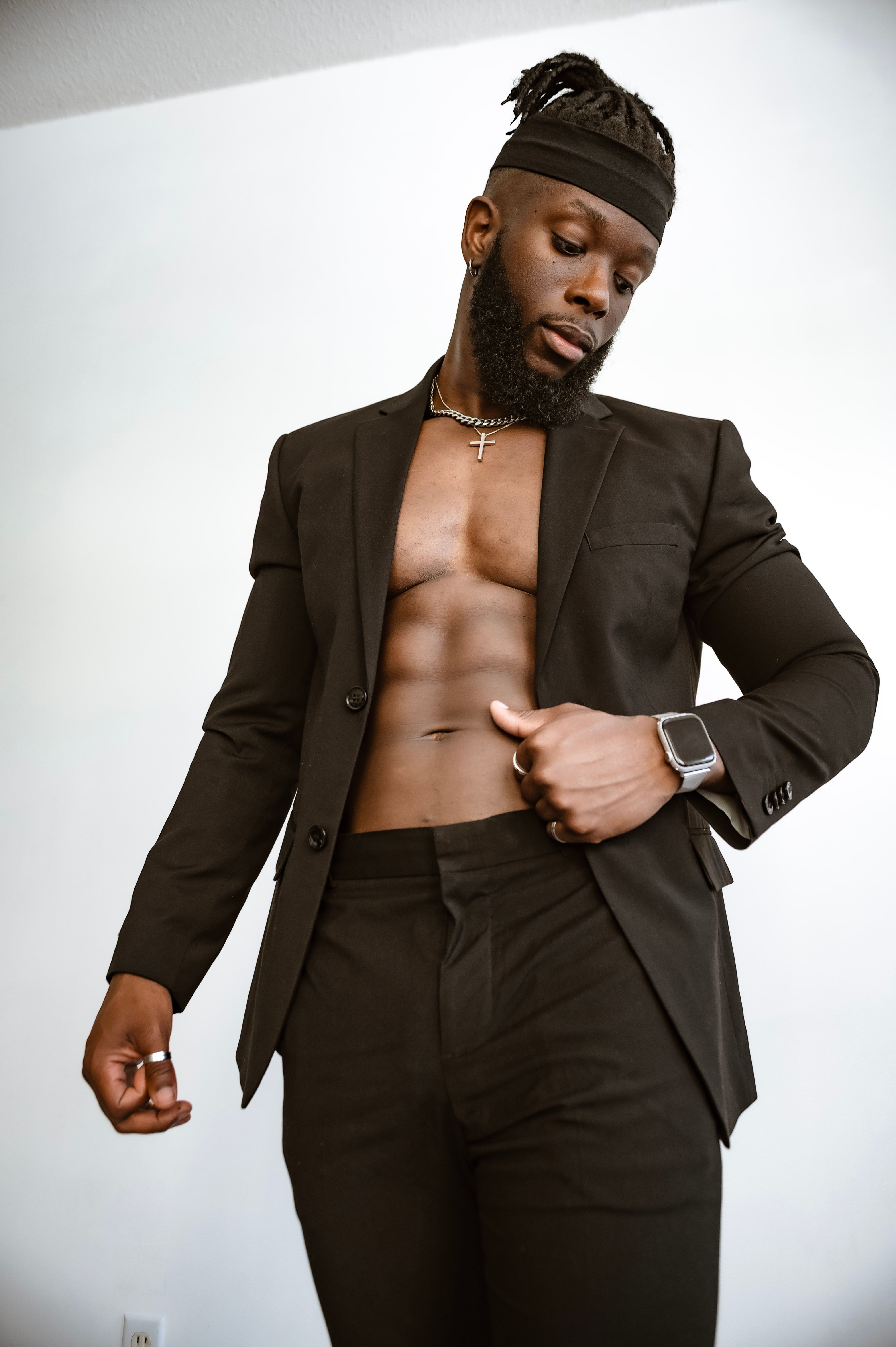 Fashionable man in a black suit showing smartwatch in a studio setting.
